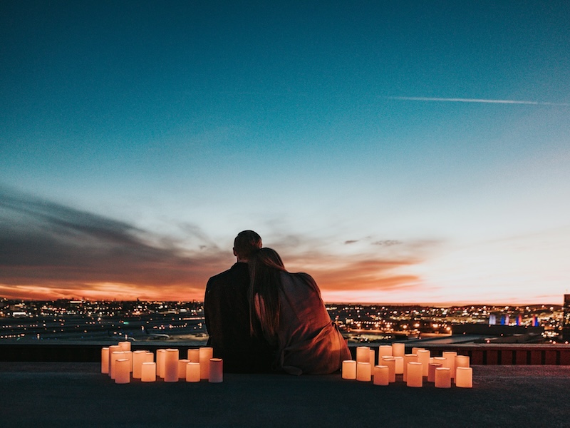 A couple on a candlelit terrace overlooking a city at dusk
